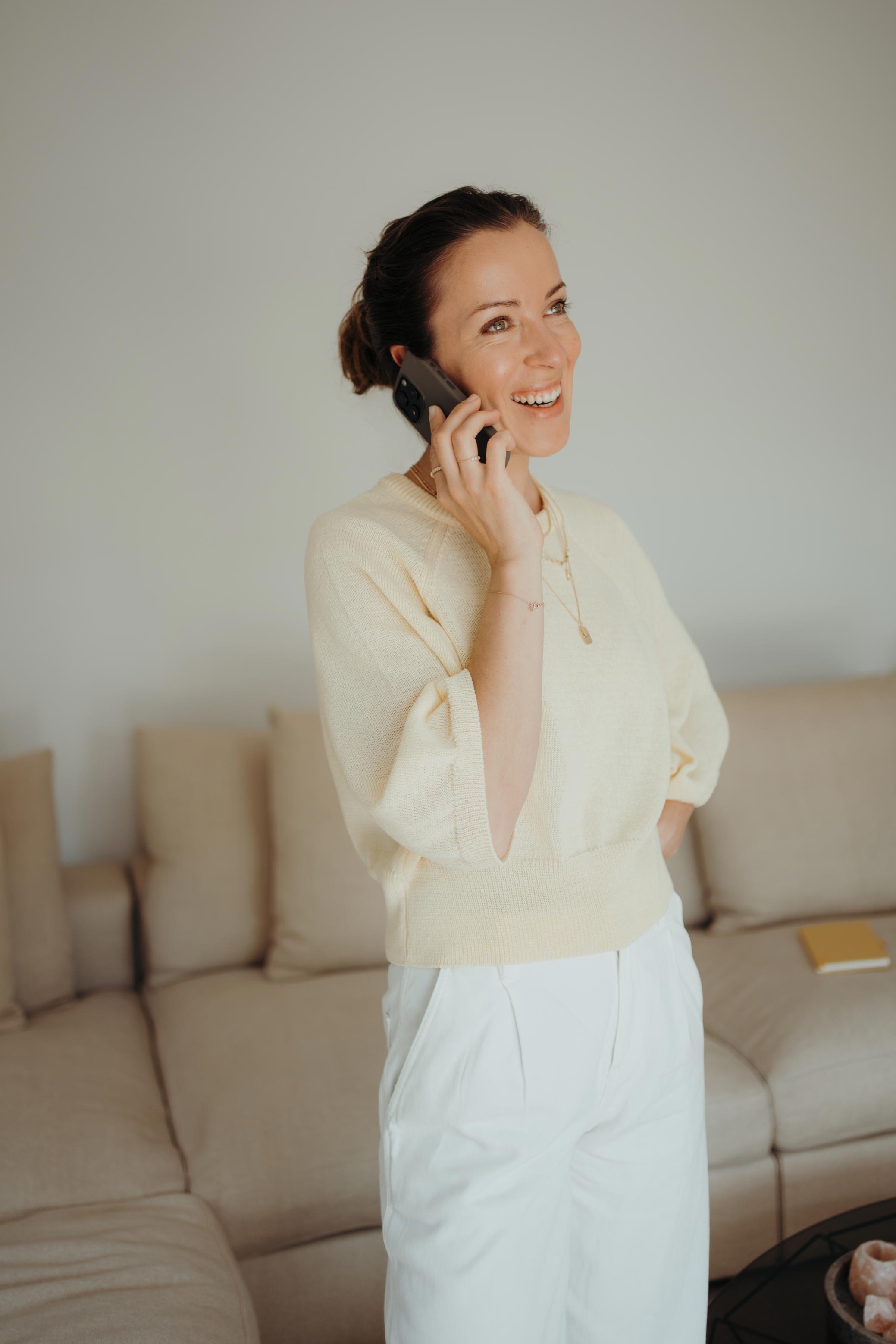 Eine lachende Frau (Dajana) spricht in einem Wohnzimmer am Telefon.
